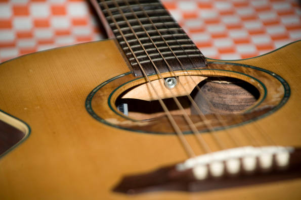 What is Keeping You From Getting Better on Your Instrument? Image of an acoustic guitar on a checkered surface