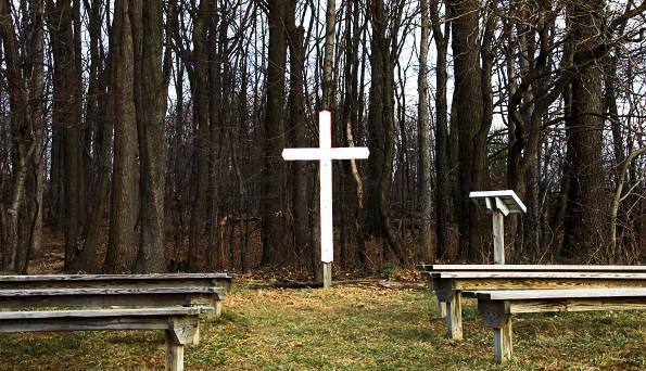 Image of an outdoor worship gathering area with a white cross as the focal piece.